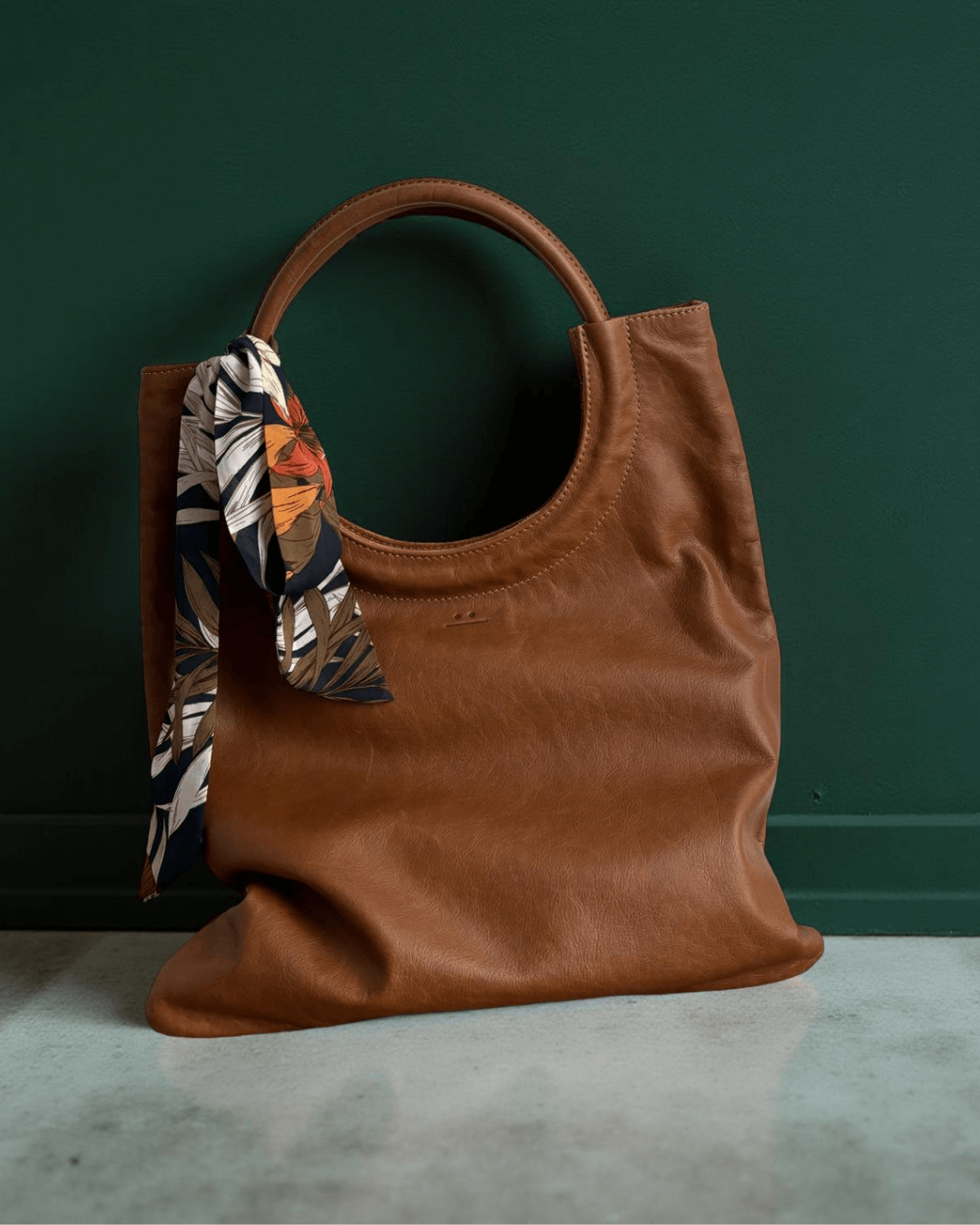 Mixed Emotions Reversible Tote in tan leather with a floral scarf, showcasing its stylish design and versatility.